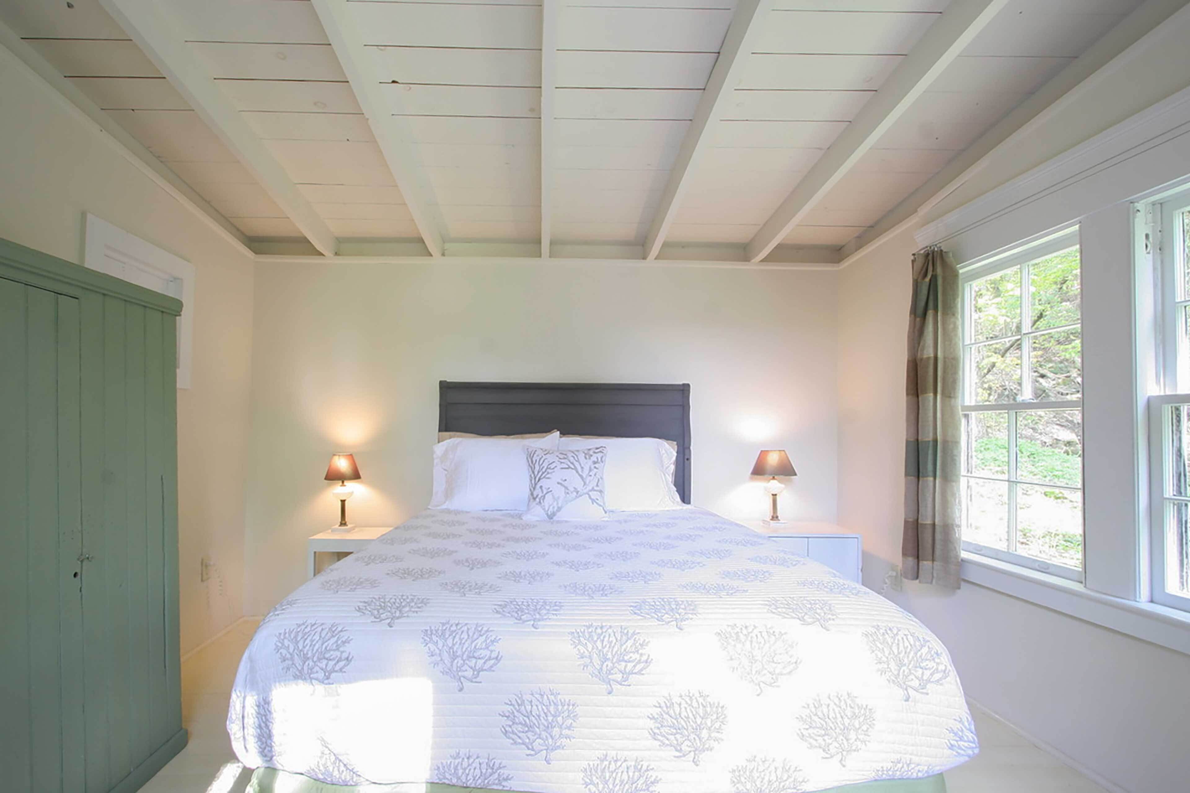 A bedroom with a bed, two bedside lamps, a window with curtains, and a green wardrobe.