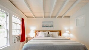 Quarto com uma cama grande, duas luminárias de cabeceira, um quadro na parede e uma janela com cortinas.