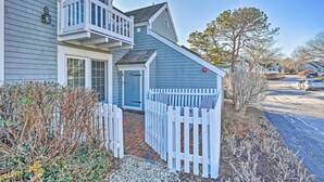 A two-story house with a balcony, a front door, and a white picket fence. - Ocean View + Beach Access: Cape Cod Townhome (Mashpee)