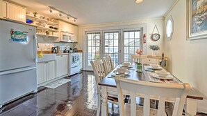 A kitchen with white cabinets, a dining table set for four, and a view through the windows. - Ocean View + Beach Access: Cape Cod Townhome (Mashpee)
