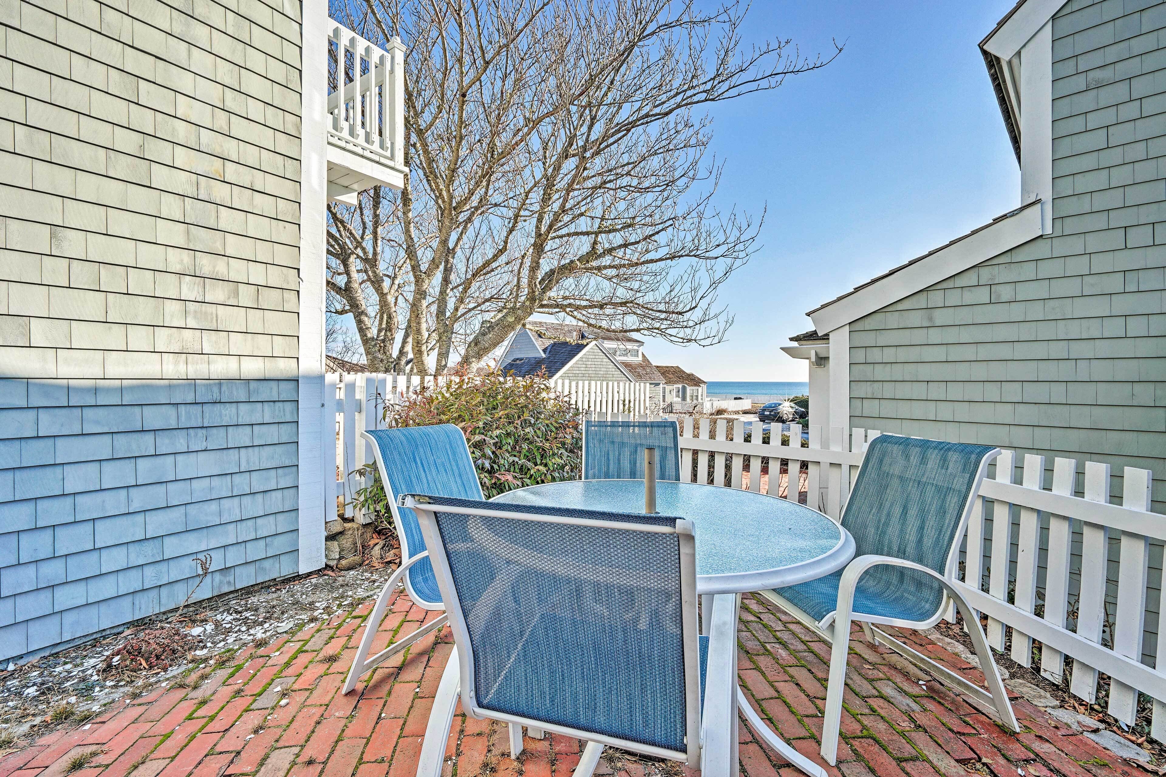 A patio with a round table and chairs, a white fence, and a view of a house with a balcony.