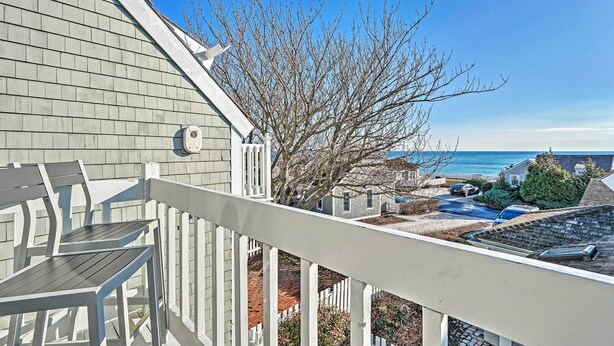A balcony with a view of a residential area, a tree, and a clear sky. - Ocean View + Beach Access: Cape Cod Townhome (Mashpee)