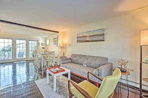 A spacious living room with a grey sofa, a coffee table, and a dining area with a white table and chairs. - Ocean View + Beach Access: Cape Cod Townhome (Mashpee)