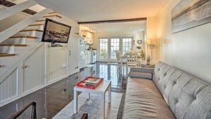 A spacious living area with a staircase, a sofa, a coffee table, and a television mounted on the wall. - Ocean View + Beach Access: Cape Cod Townhome (Mashpee)