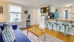 A compact living space with a sofa, a coffee table, a kitchen area with a TV, and a dining area with bar stools. - 1 Mi to Ferry: 'sea Street Cottage' in Hyannis (Hyannis)