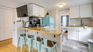 A compact kitchen with white cabinets, a blue refrigerator, a wooden countertop, and three bar stools. - 1 Mi to Ferry: 'sea Street Cottage' in Hyannis (Hyannis)