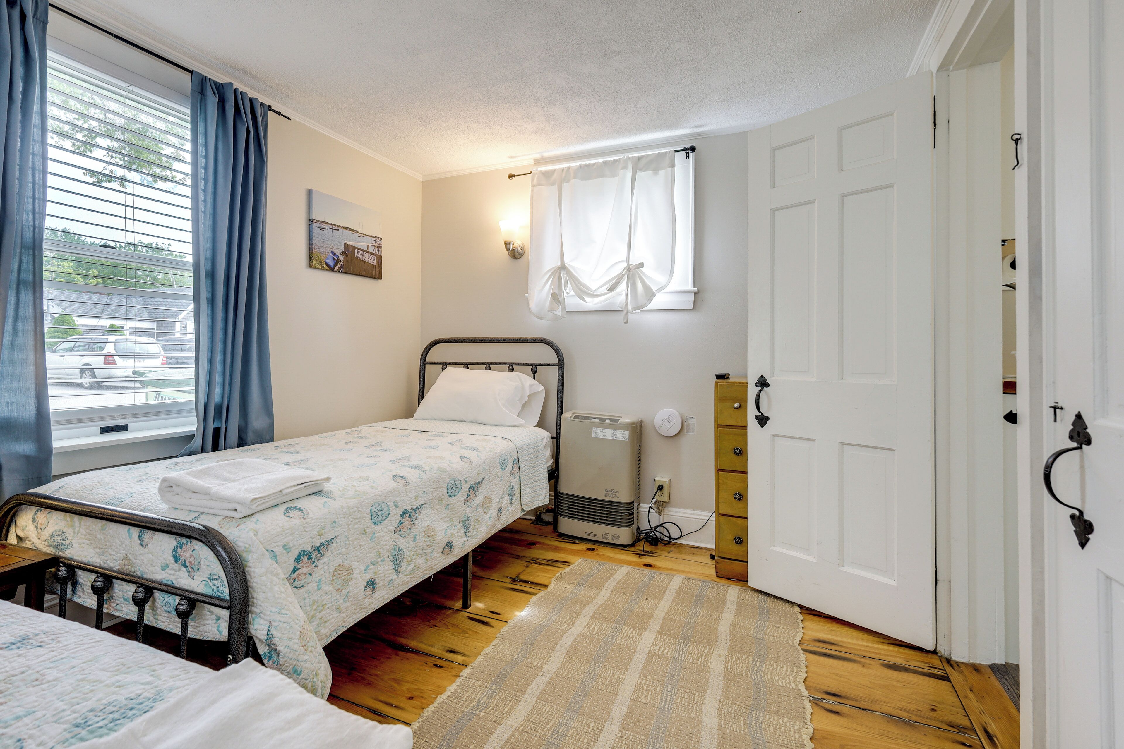 Ein Schlafzimmer mit Bett, Heizung, Fenster mit Vorhängen und einer Tür.