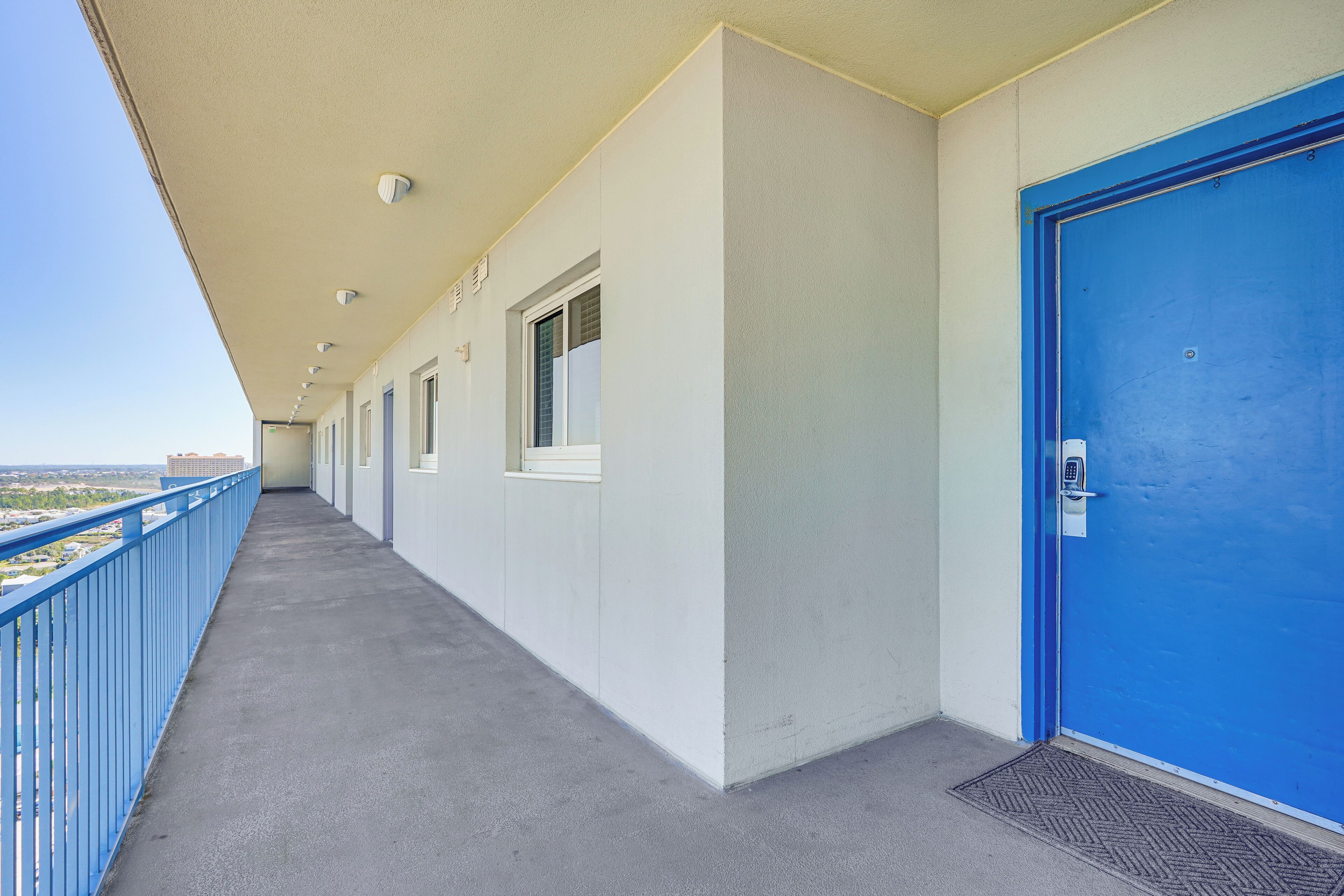 A long corridor with a blue railing, a blue door, and windows along the walls.
