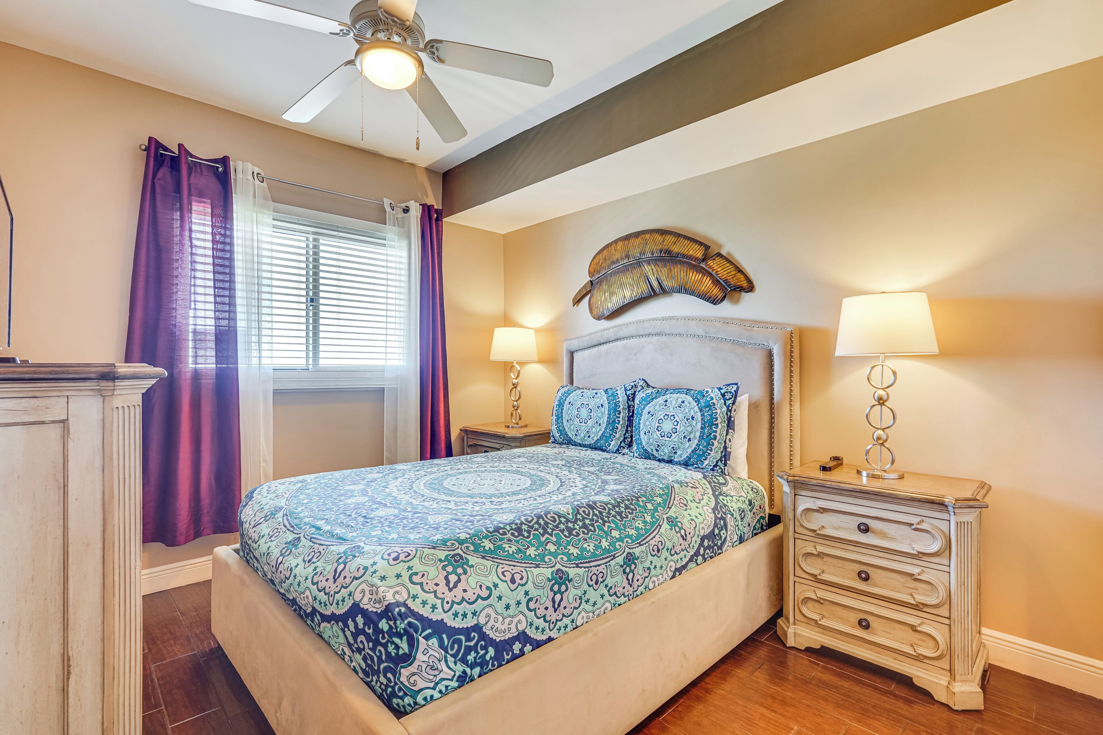 A bedroom with a bed, two bedside tables with lamps, a ceiling fan, and a window with curtains.