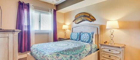 A bedroom with a bed, two bedside tables with lamps, a ceiling fan, and a window with curtains.