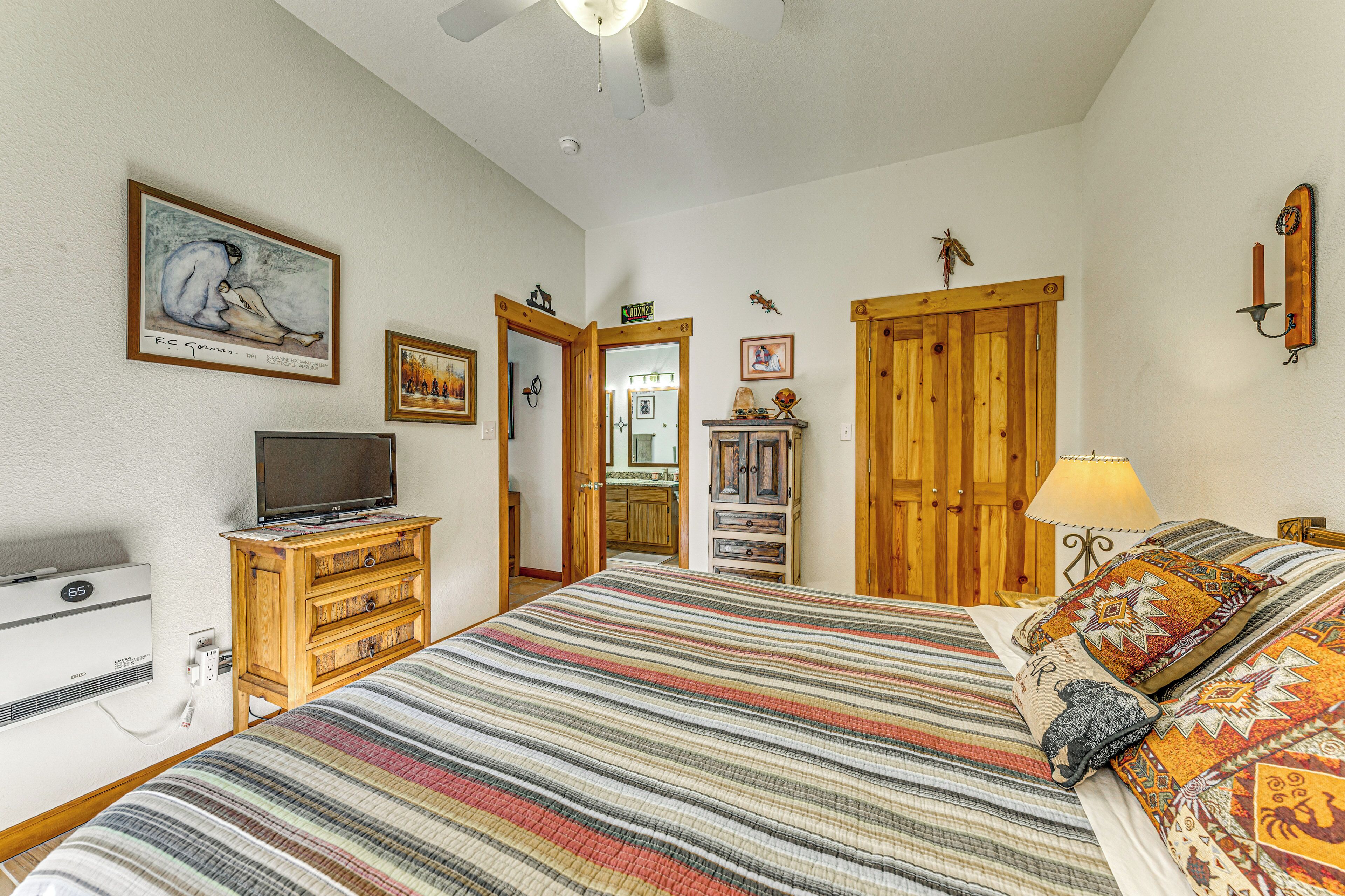 A bedroom with a bed, wooden dresser, television, and a door leading to a kitchen.