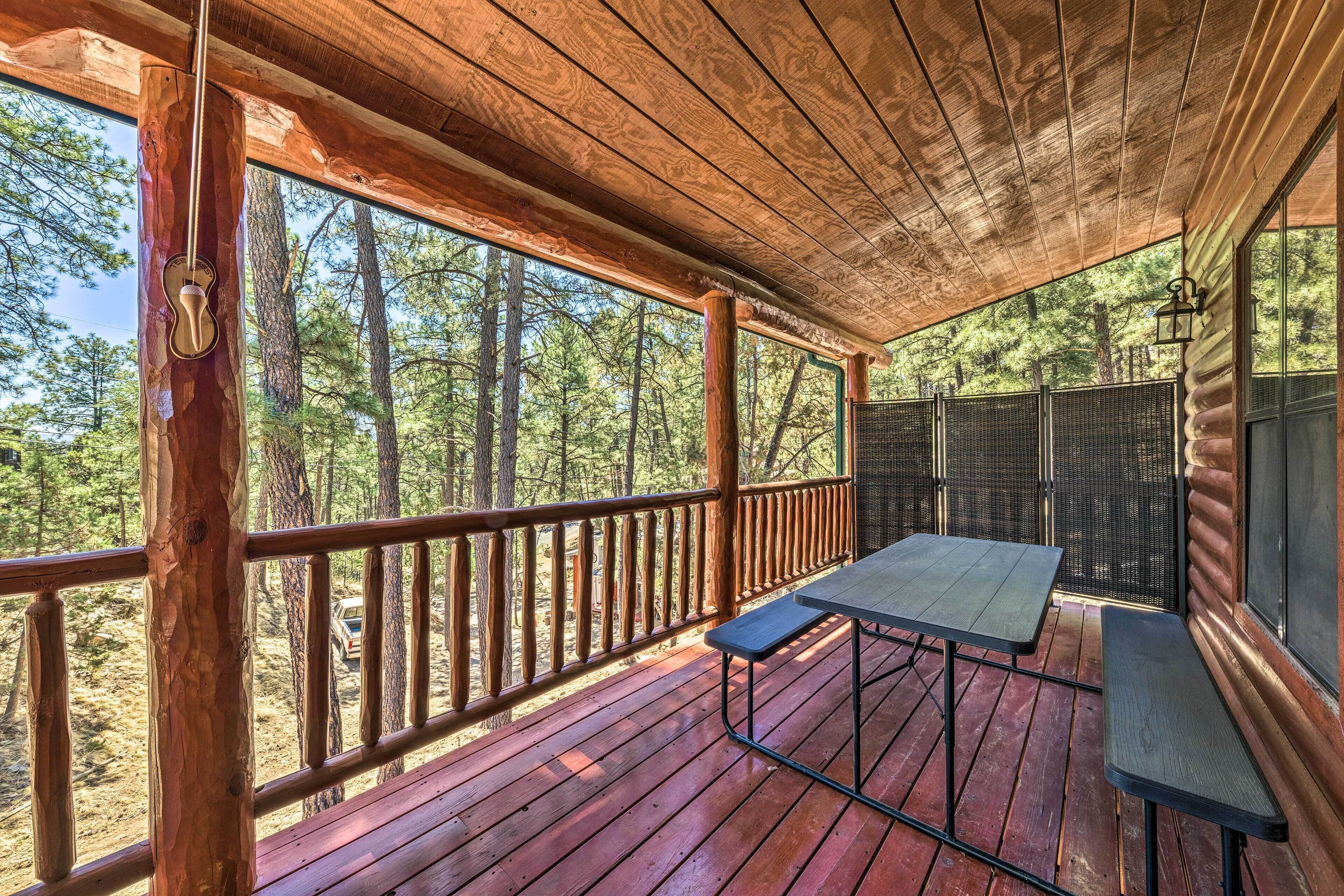A wooden deck with a table and benches, overlooking a forested area.