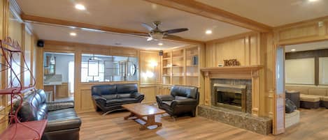 A spacious living room with a fireplace, leather sofas, a coffee table, and a ceiling fan.
