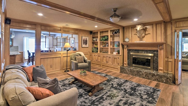 A spacious living room with a fireplace, wooden paneling, and a cozy seating area. - Lake Access & Pool: Spacious Freeport Home! (Freeport)