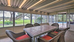 A covered patio with a table and wicker chairs, large windows, and a view of a golf course. - Lake Access & Pool: Spacious Freeport Home! (Freeport)