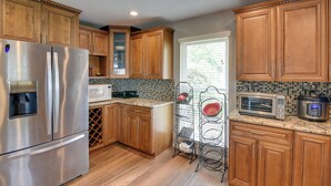 A kitchen with wooden cabinets, stainless steel appliances, a wine rack, and a window with blinds. - Lake Access & Pool: Spacious Freeport Home! (Freeport)