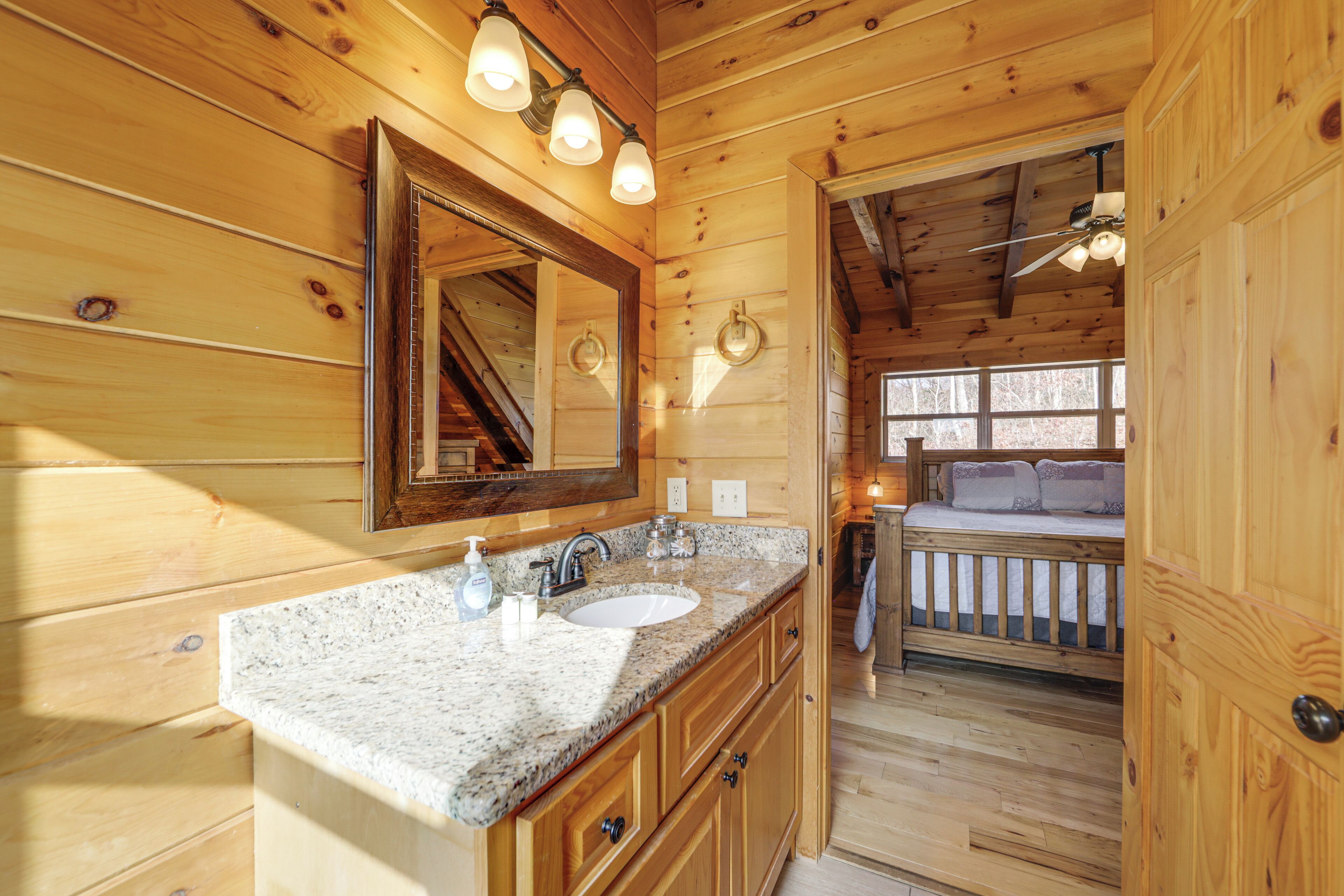 Un baño de cabaña de madera con lavamanos de encimera de granito, un espejo grande y un ventilador de techo.