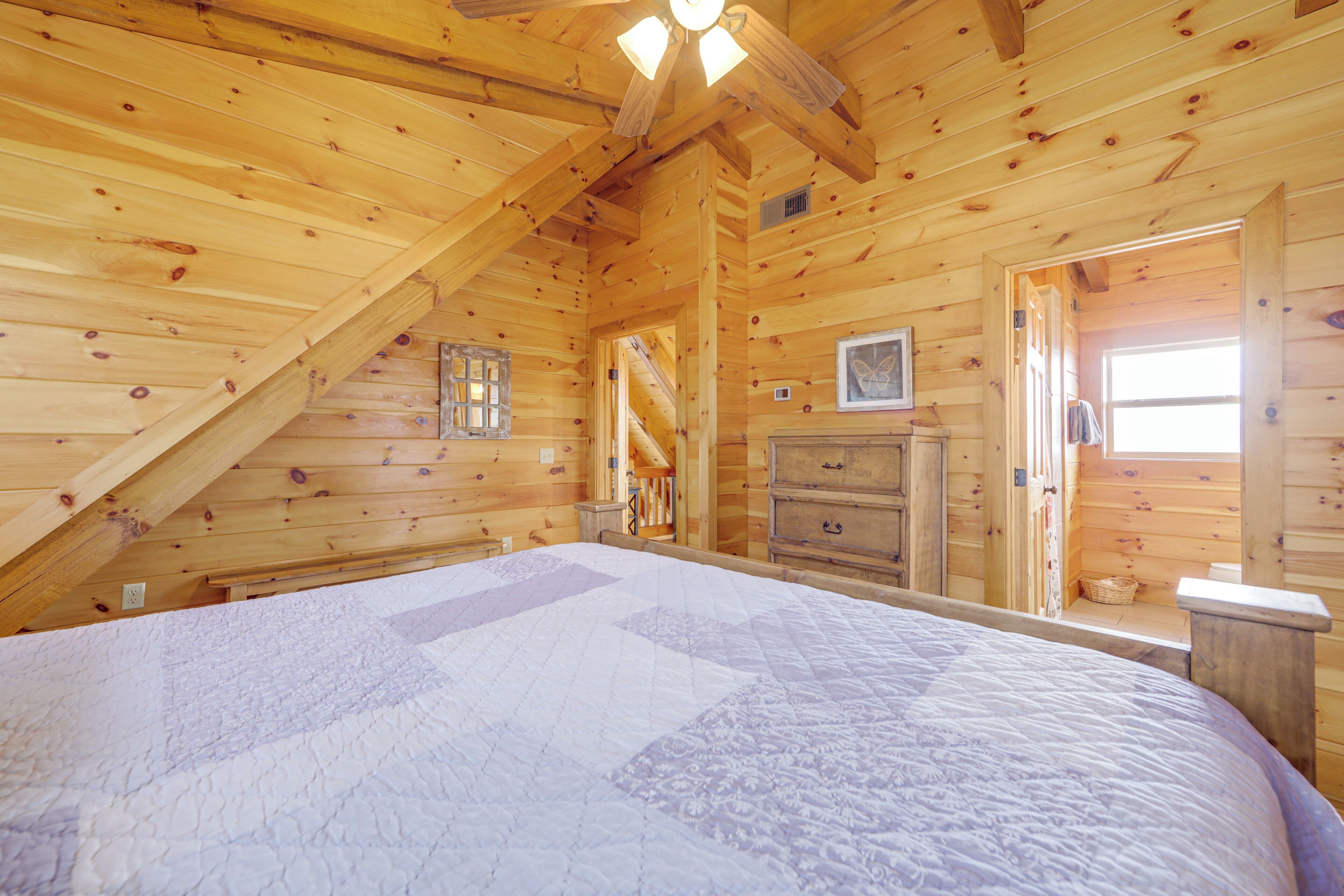 A wooden cabin bedroom with a large bed, a dresser, and a window.