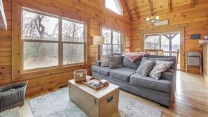 A cozy cabin interior with a wooden interior, a gray sofa, a coffee table, and large windows offering a view of the forest. - Elevated Cabin Bordering Smoky Mountain Nat'l Park (Bryson City)