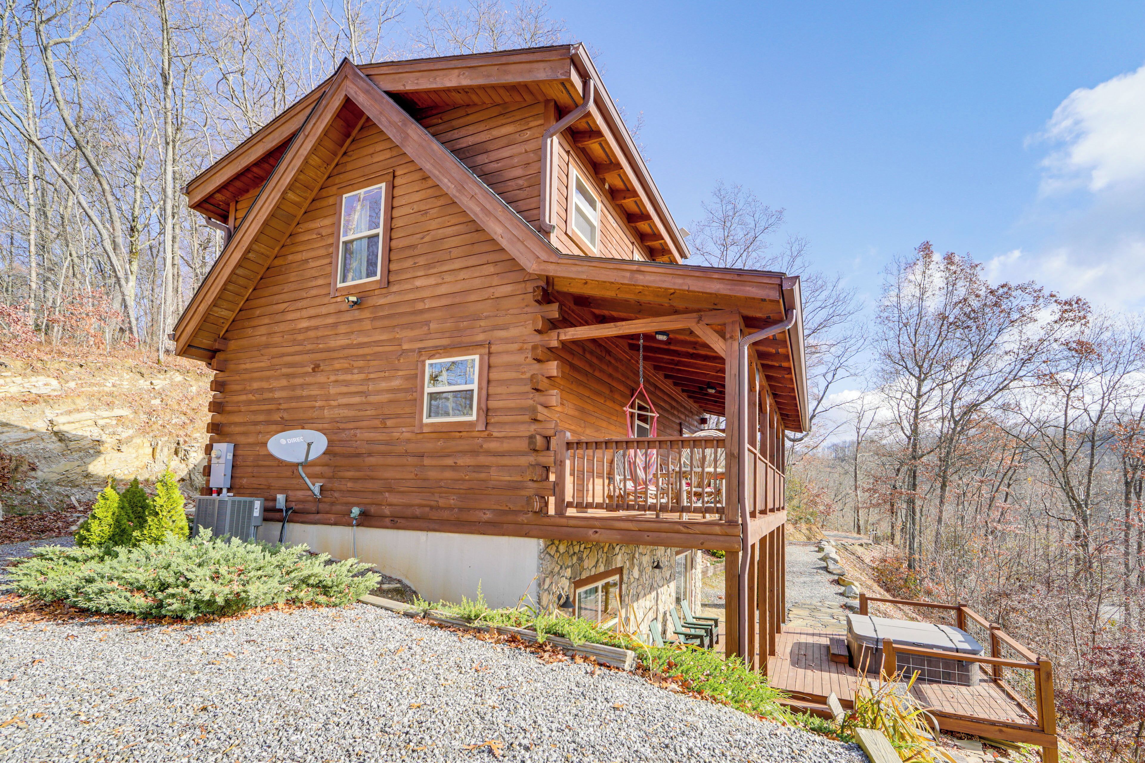 A wooden cabin with a balcony, a stone foundation, and a gravel driveway.