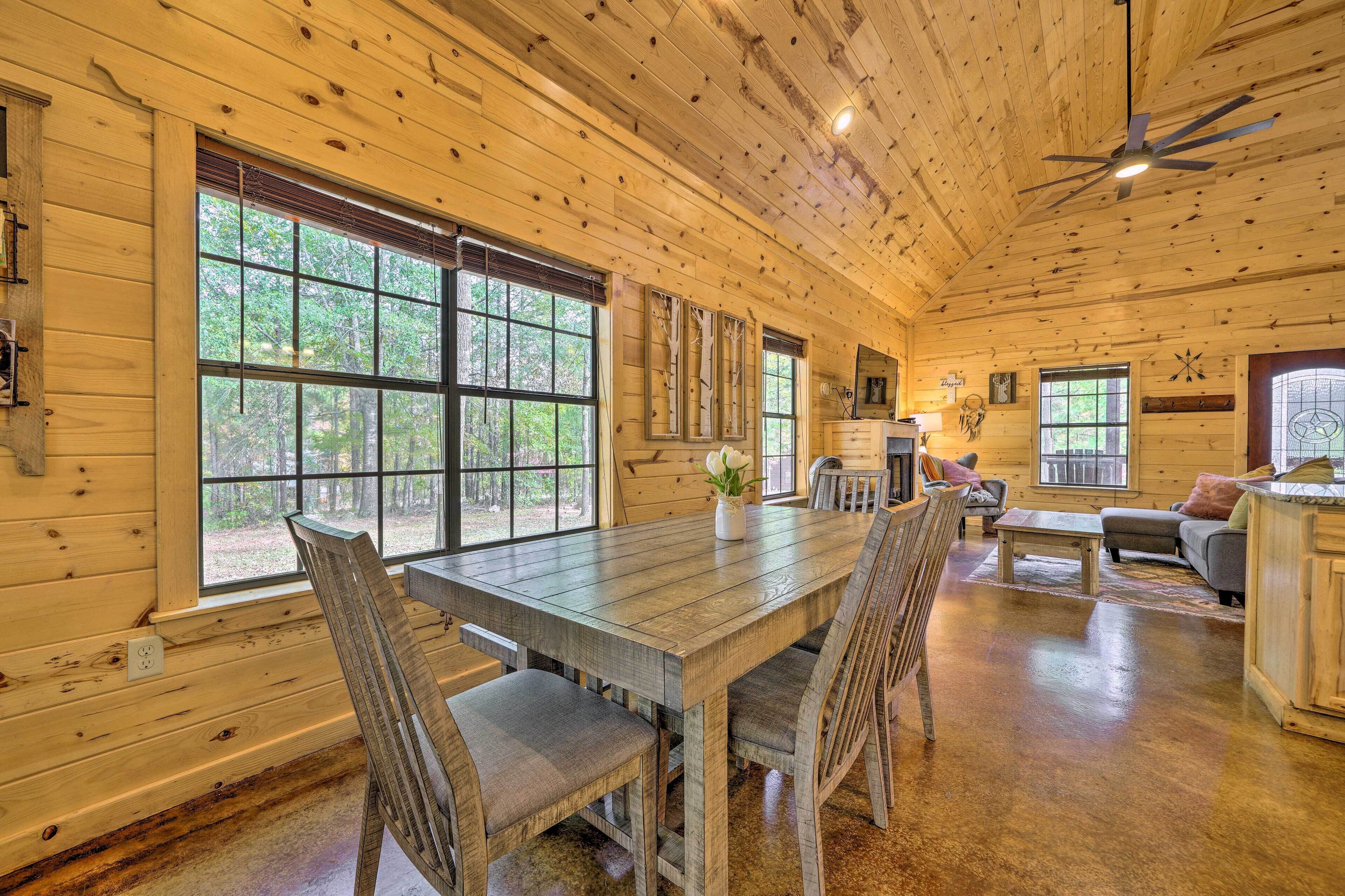 A wooden cabin interior with a dining table, chairs, a sofa, and a ceiling fan.
