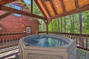 A wooden cabin with a hot tub on a wooden deck, surrounded by trees.
