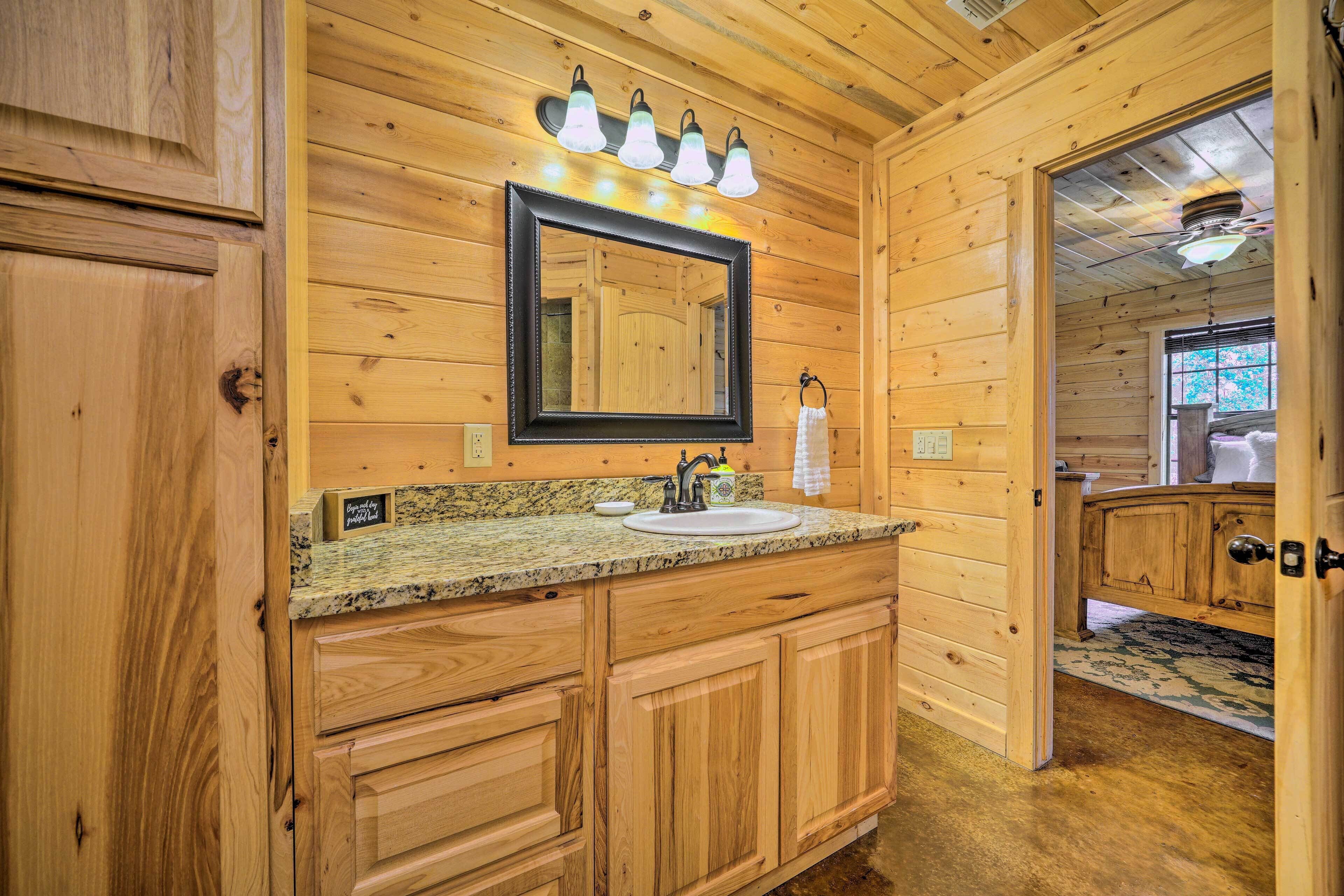 A wooden cabin bathroom with a granite countertop sink, wooden cabinets, a large mirror, and a ceiling fan.