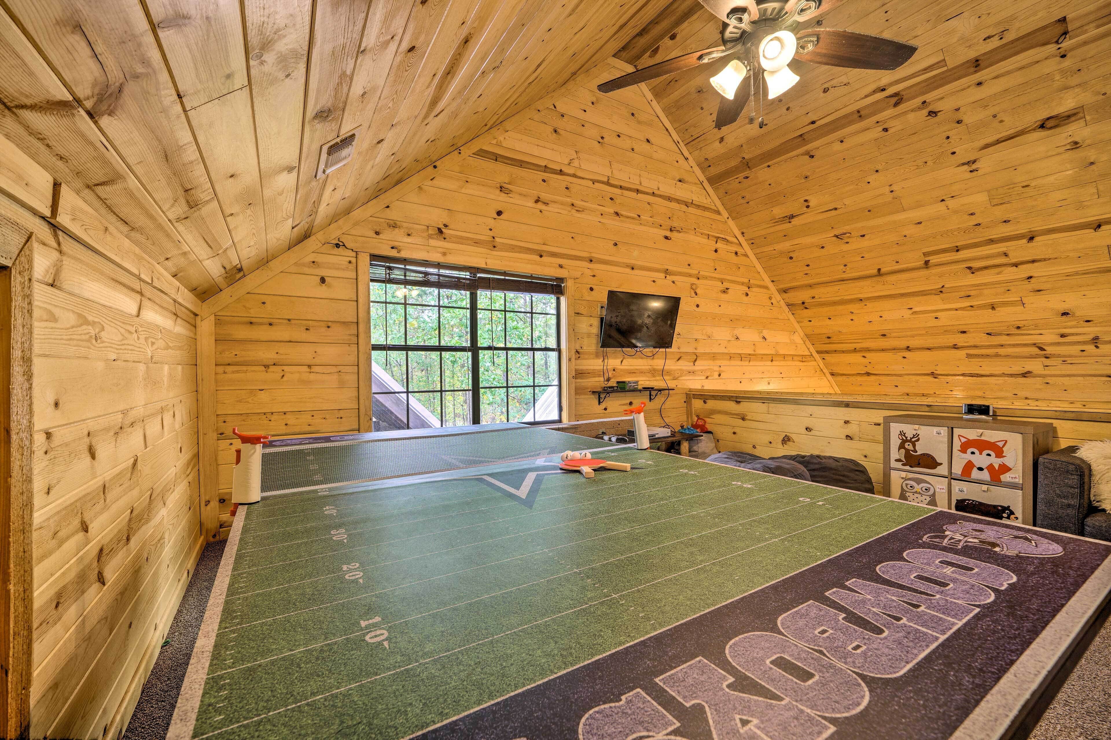 A ping pong table in a wooden room with a sloped ceiling and a window.