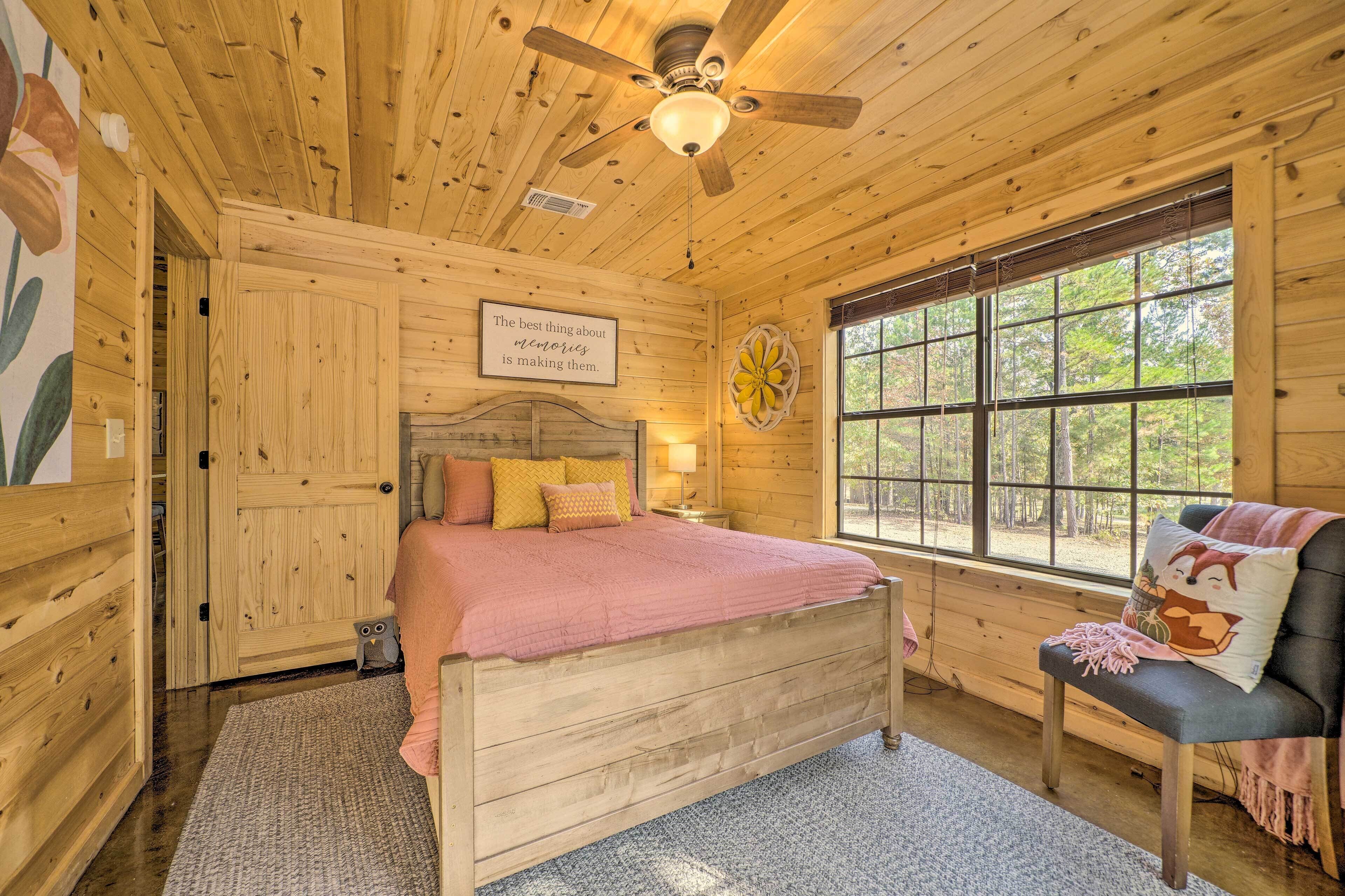 Une chambre dans une cabane en bois, avec un lit, une chaise, une fenêtre et un ventilateur de plafond.