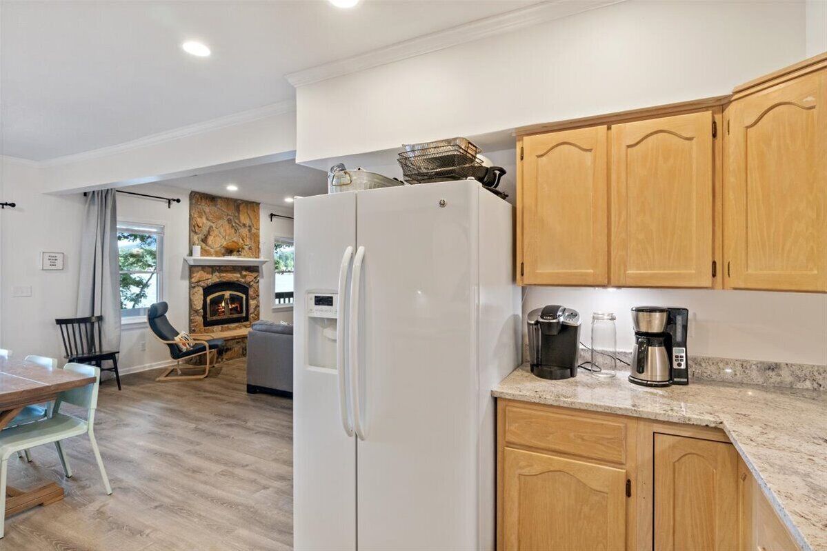 A modern kitchen with wooden cabinets, a white refrigerator, and a stone fireplace.