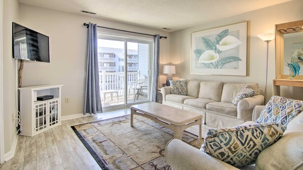 A living room with a sofa, coffee table, and a flat-screen TV. There is a balcony with a view of buildings.