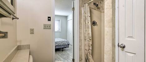 Un baño con bañera, ducha y una puerta que da a un dormitorio.