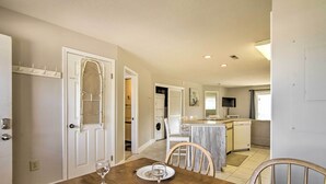 A dining area with a wooden table and chairs, a kitchen in the background, and a door with a decorative grille.