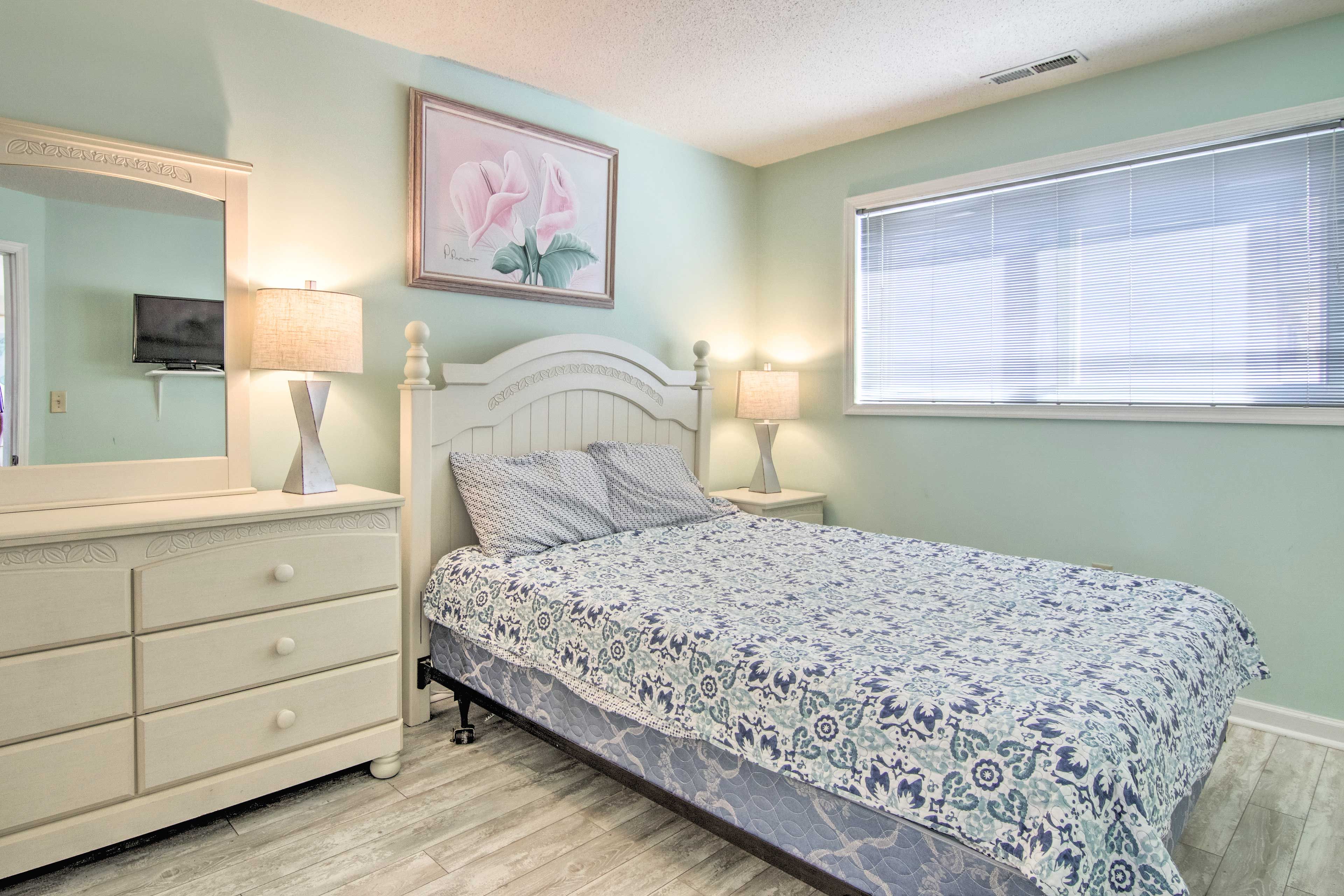 A bedroom with a bed, a dresser, a mirror, a painting, and a window with blinds.