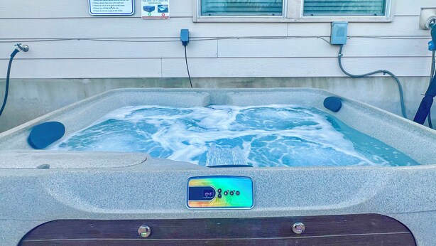 Un jacuzzi con pantalla digital que muestra la temperatura, conectado a una toma de corriente en la fachada de una casa.