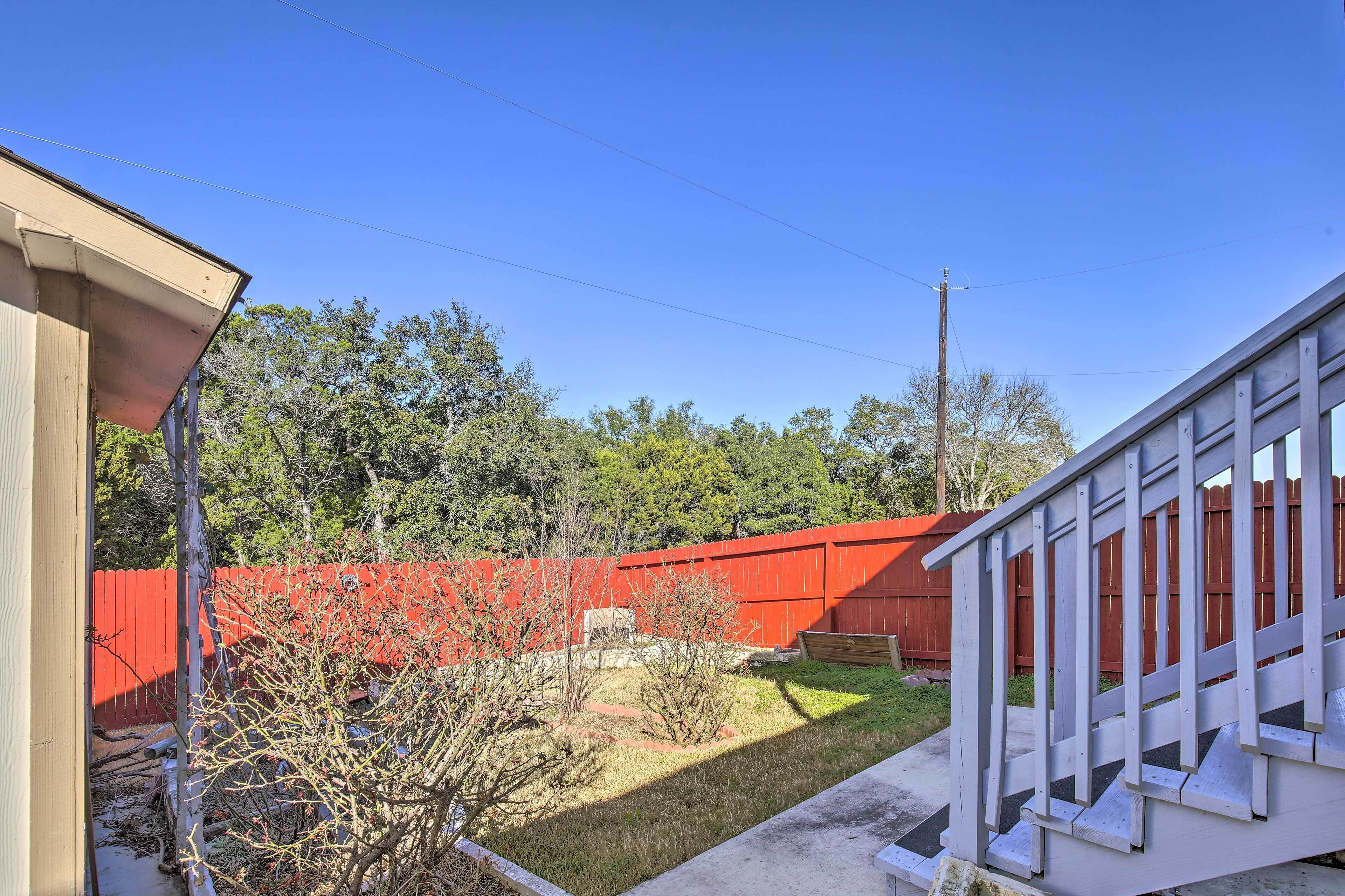 A residential backyard with a red fence, a small tree, and a concrete staircase.