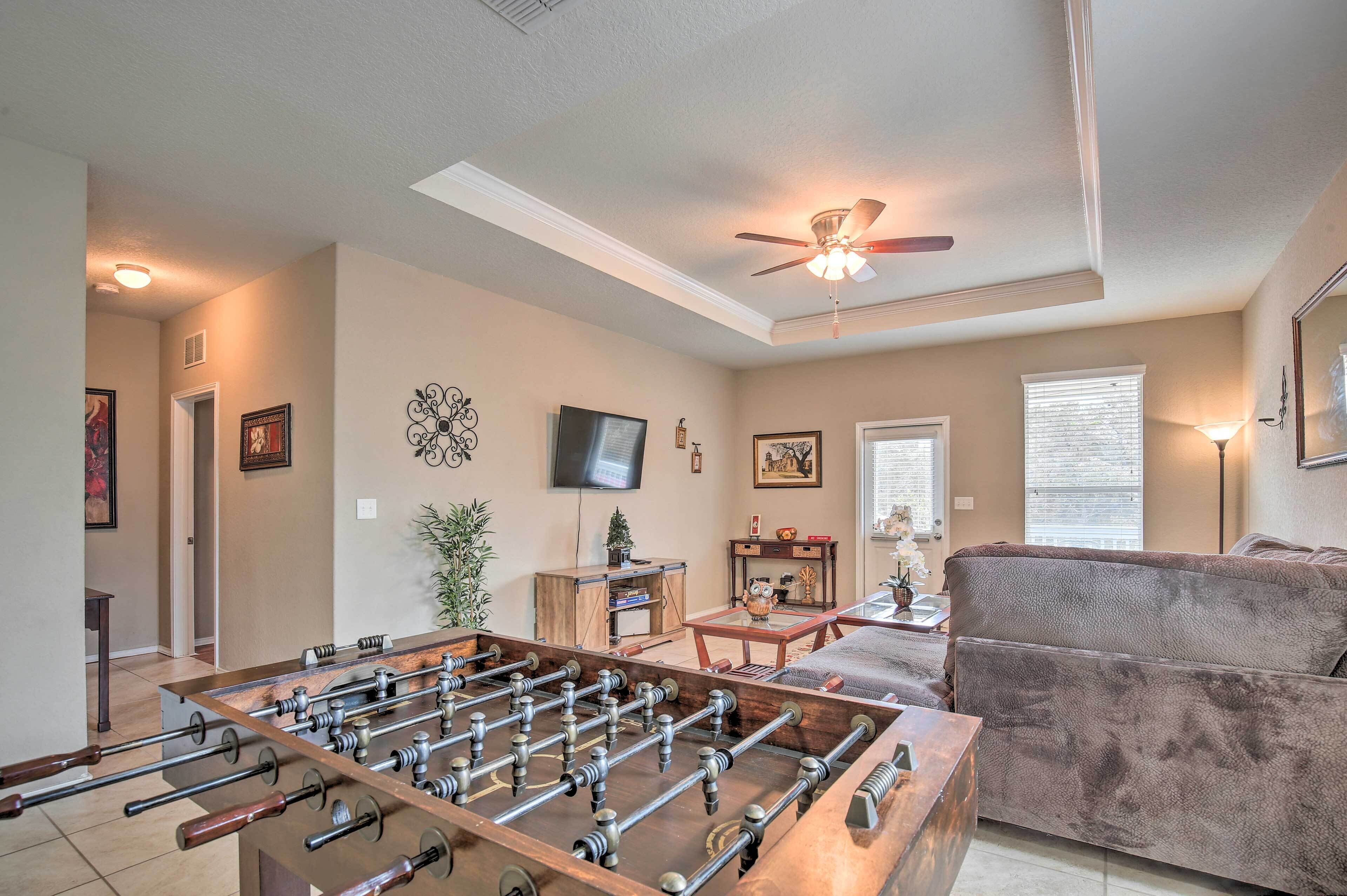 A living room with a foosball table, a sofa, a ceiling fan, and a television on the wall.