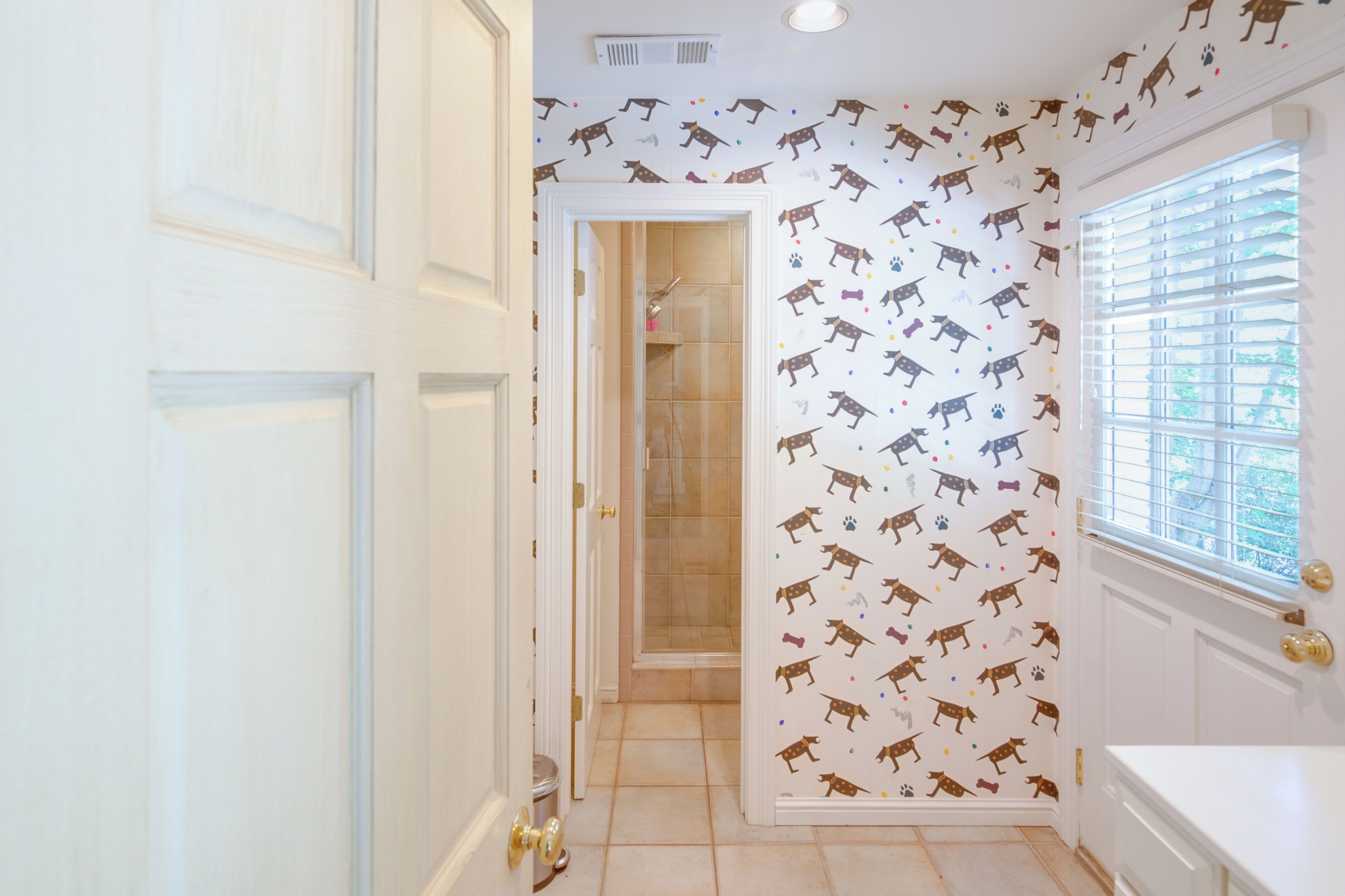 A hallway with patterned wallpaper, a door, and a window with blinds.