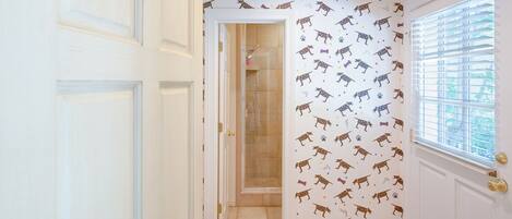 A hallway with patterned wallpaper, a door, and a window with blinds.