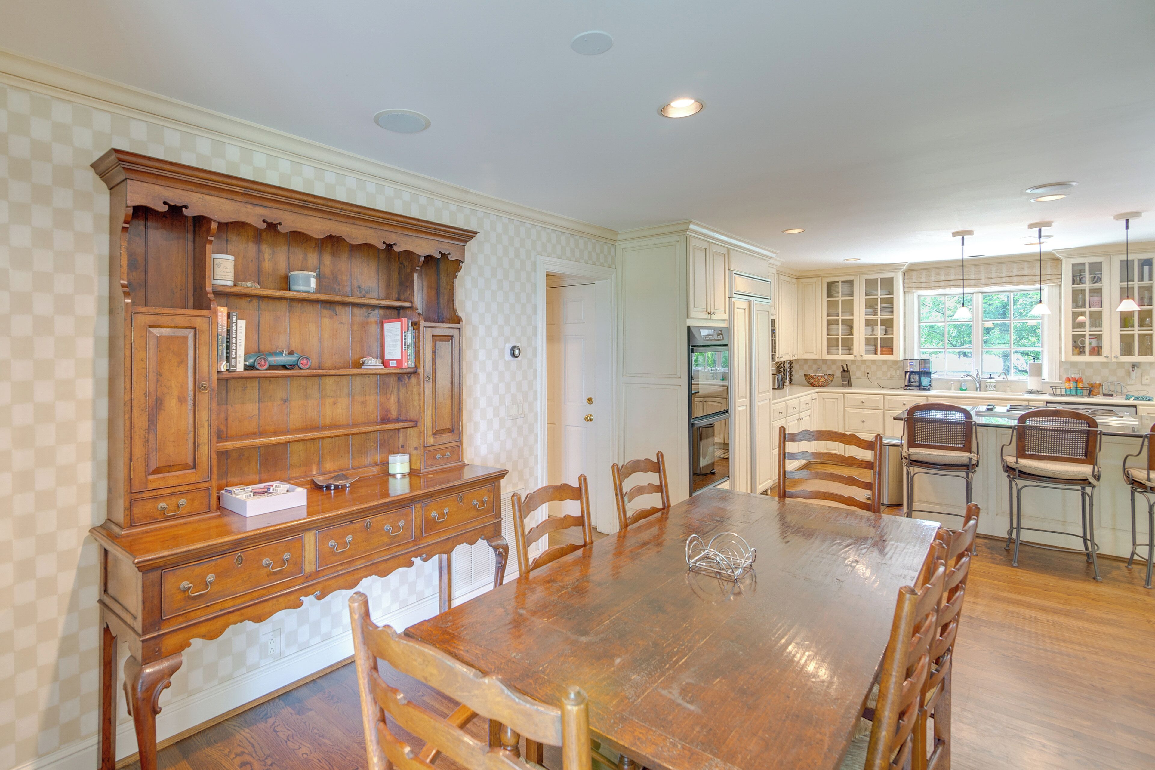 A spacious dining area with a large wooden table and chairs, surrounded by wooden cabinetry and a kitchen in the background.