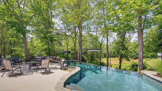 An outdoor swimming pool with a curved edge, surrounded by a patio area with chairs and a table. - Pool, Hot Tub & Outdoor Theater: Franklin Retreat (Franklin)