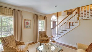 A living room with a glass coffee table, two patterned armchairs, a beige sofa, a staircase with wooden railings, and a large window with curtains. - Pool, Hot Tub & Outdoor Theater: Franklin Retreat (Franklin)