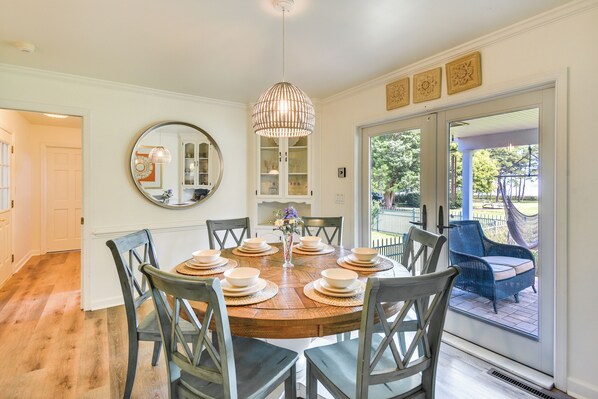 A dining area with a wooden table set for six, surrounded by chairs, a hanging light fixture, and a large mirror on the wall.