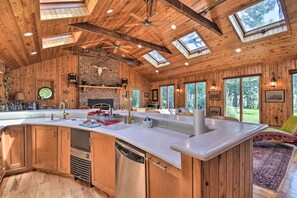 A spacious kitchen with wooden cabinets, a large island, skylights, and a brick wall.
