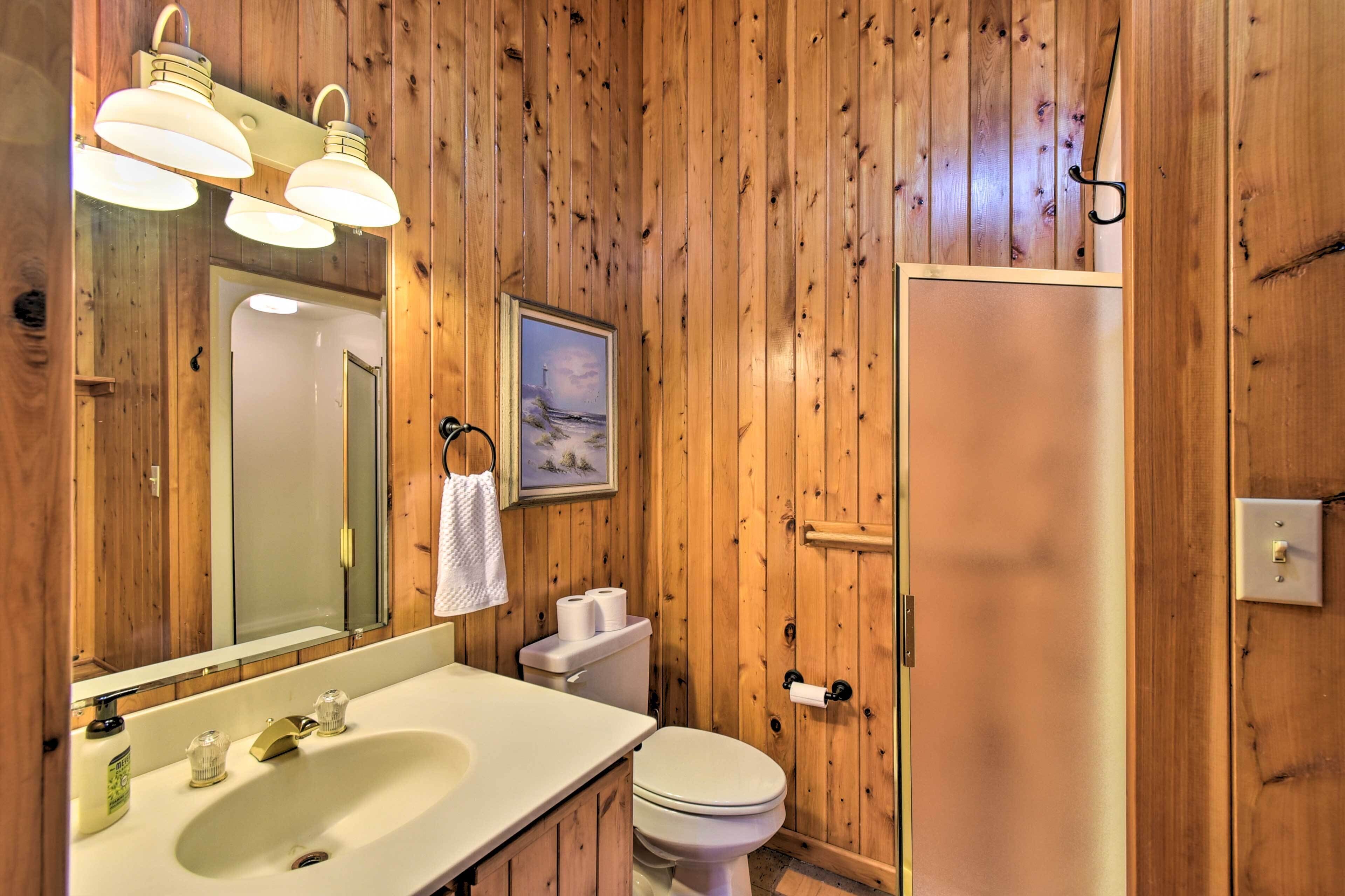 Une salle de bain aux murs lambrissés, équipée d’un lavabo, de toilettes et d’une douche.