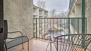 A balcony with a view of a multi-story building, a metal railing, and a table with chairs.