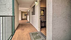 A narrow hallway with a textured wall, a green metal railing, and a doormat at the entrance.