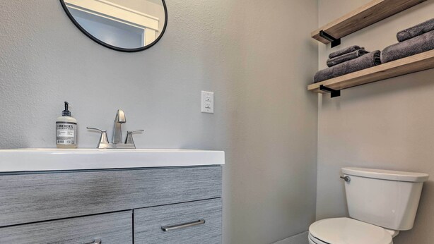 Een badkamer met een witte wastafel, grijze lades, een wit toilet en houten planken met handdoeken.