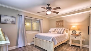 Un dormitorio con cama, ventilador de techo, mesita de noche, lámpara y ventana con persianas.