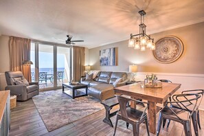 A spacious living room with a leather sofa, a dining table with chairs, a ceiling fan, and a large window with curtains.
